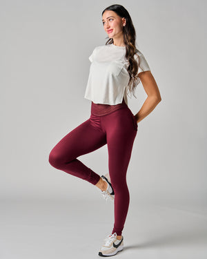 Woman wearing a white top and maroon leggings on a gray background
