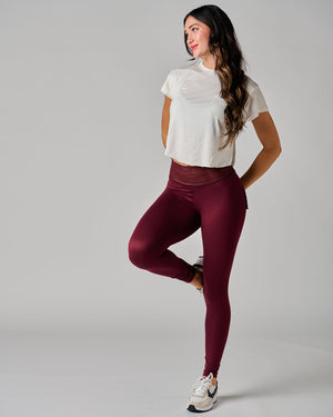Woman wearing a white crop top and maroon leggings on a gray background