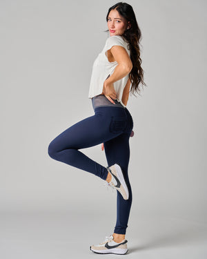 Woman wearing navy leggings and a white top on a gray background