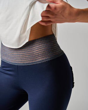 Person wearing a white top and blue leggings with a textured waistband against a light gray background