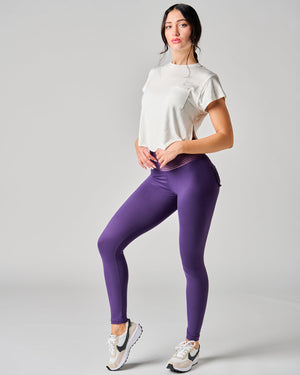 Woman wearing a white t-shirt and purple leggings on a gray background