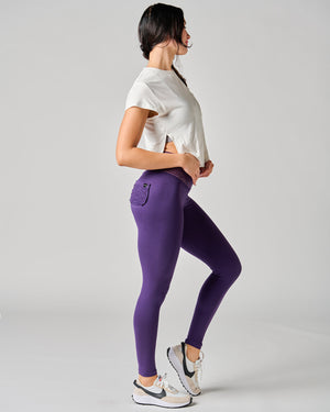 Woman wearing a white crop top and purple leggings on a gray background