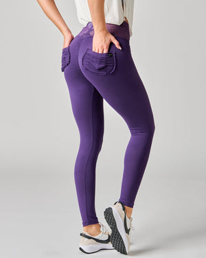 Purple leggings with front pockets worn by a person on a gray background