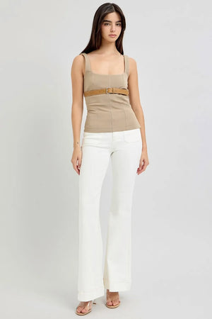 Woman wearing a beige tank top with a belt and white pants on a white background