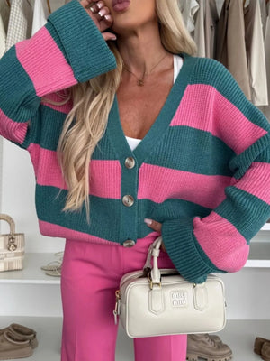 Person wearing a pink and teal striped cardigan with pink pants, holding a beige handbag.