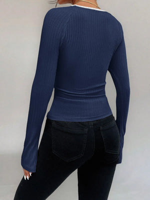 Person wearing a blue ribbed long-sleeve top and black pants on a plain background