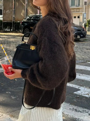 Person holding a black handbag and a red drink on a street.