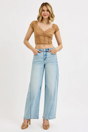Woman wearing a brown lace top and light blue jeans on a white background