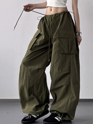 Person wearing olive green baggy pants with a white top on a plain background