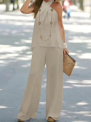 Woman wearing a beige outfit with wide-leg pants and a top, holding a straw bag on a street.