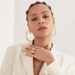 A woman wearing four gold rings on her finger and 2.5" Skylar Hoops in her ears