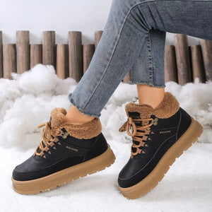 Black winter boots with brown fur and soles worn by a person in snow.