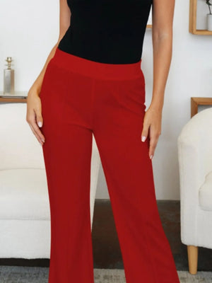 Person wearing red pants and a black top in a room with white walls and furniture.