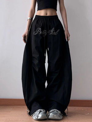 Person wearing black wide-leg pants with 'Pitty Girl' text, standing against a plain background.