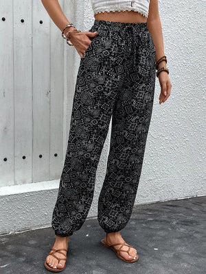 Person wearing black patterned pants against a gray wall.