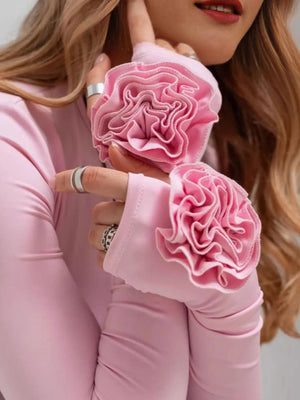 Person wearing pink fingerless gloves with floral designs, holding one glove to the camera.