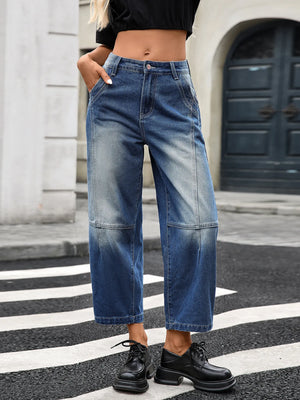 Person wearing blue jeans and black shoes on a city street.