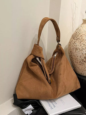 Brown suede handbag on a surface with a neutral background