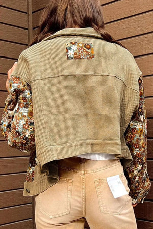 Person wearing a beige vest over a floral shirt with a wooden background