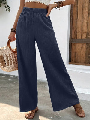 Person wearing navy wide-leg pants with a white top and straw bag against a wooden door background.