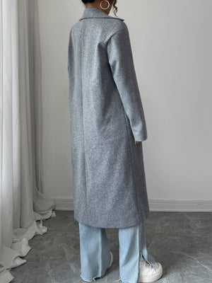 Person wearing a long gray coat in a minimal indoor setting