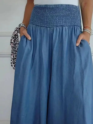 Person wearing a blue smocked waist skirt with hands in pockets against a white background