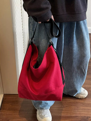 Red handbag held by a person wearing jeans and white shoes on a wooden floor.