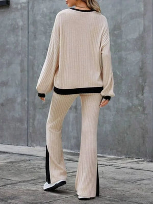 Person wearing a beige ribbed sweater and pants with black trim against a gray wall.