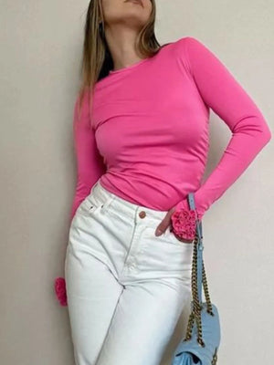Person wearing a bright pink long-sleeve top and white pants, holding a blue handbag.