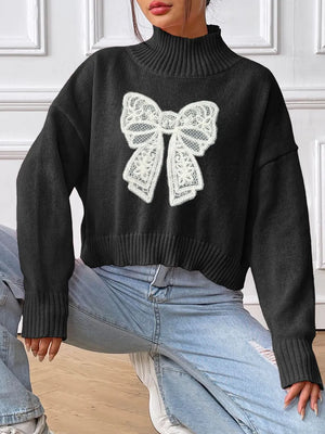 Black sweater with a large white lace bow design worn by a person.