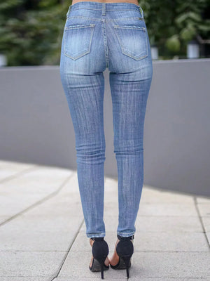 Person wearing blue jeans standing on a sidewalk with a blurred background