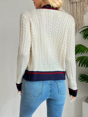 Person wearing a cream cable knit sweater with blue and red accents and blue jeans.