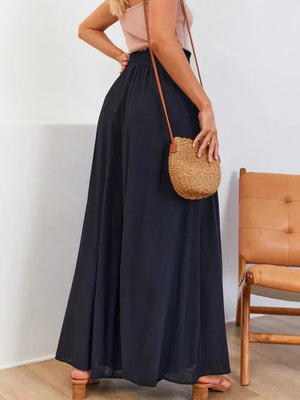 Person wearing a long black skirt holding a woven bag in a minimal indoor setting.