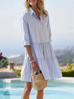 Woman in a light blue dress holding a straw bag by a pool