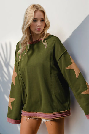 Woman wearing a green sweatshirt with star patterns against a white wall.
