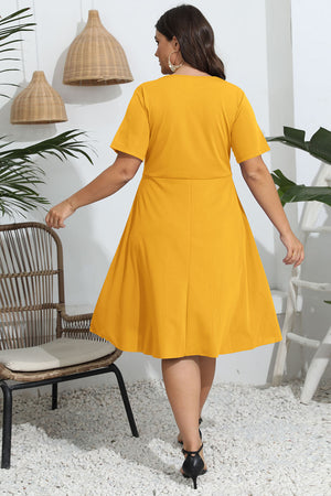 Woman wearing a yellow dress in an indoor setting with plants and a chair.