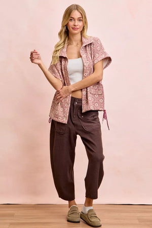 Woman wearing a patterned shirt and brown pants on a pink background
