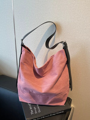 Pink handbag with black strap on a book against a neutral wall