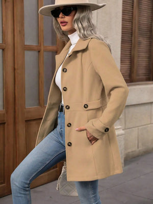 Woman wearing a beige coat, sunglasses, and a hat in an urban setting.