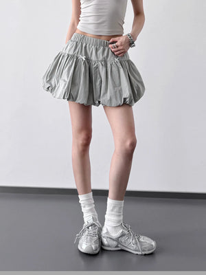 Person wearing a gray pleated skirt, white top, and silver sneakers on a plain background