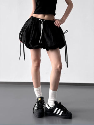 Person wearing a black drawstring skirt with white socks and black Adidas shoes on a plain background