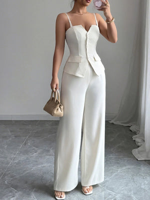 Woman wearing a white jumpsuit with a matching jacket, holding a beige handbag indoors.