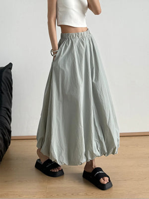 Person wearing a light green skirt and white top in a minimalistic setting.
