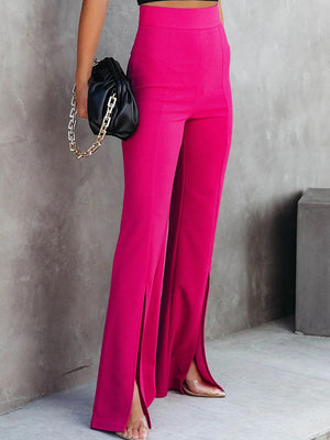 Person wearing bright pink pants with a high slit, standing against a gray concrete wall.