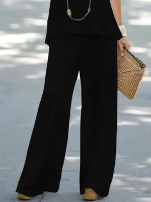 Person wearing black wide-leg pants holding a woven clutch on a light background
