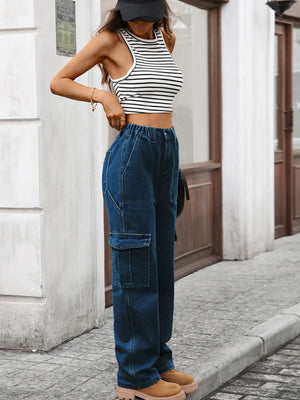 Person wearing a black and white striped crop top and blue cargo pants standing against a building.
