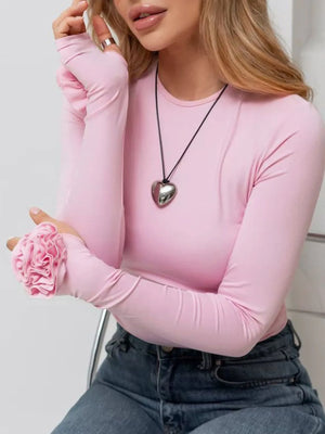 Person wearing a pink long-sleeve top with a heart-shaped necklace and holding a pink flower.