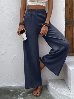Person wearing navy wide-leg pants and a white top, holding a coffee cup against a white wall.