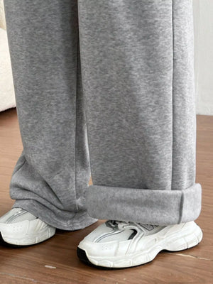 Gray sweatpants being worn with white sneakers on a wooden floor.