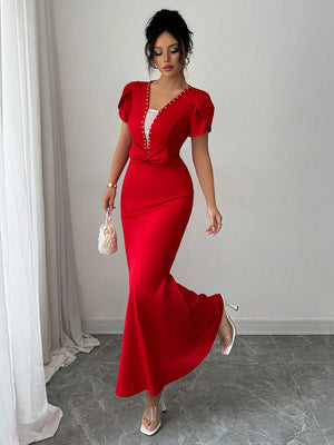 Woman in a red evening gown standing in a room with white walls and gray floor.